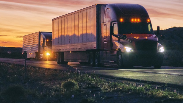 Two Semi-trailer trucks driving in the sunset